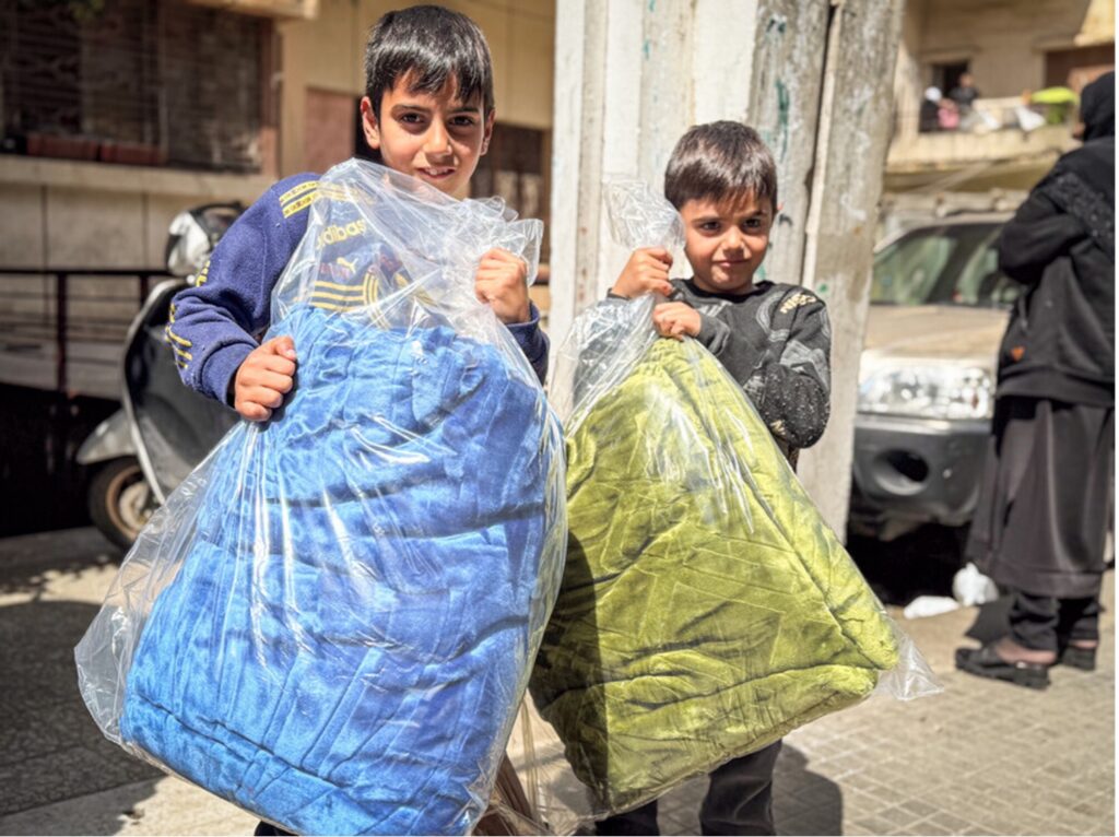 Two young boys hold blankets in plastic bags.